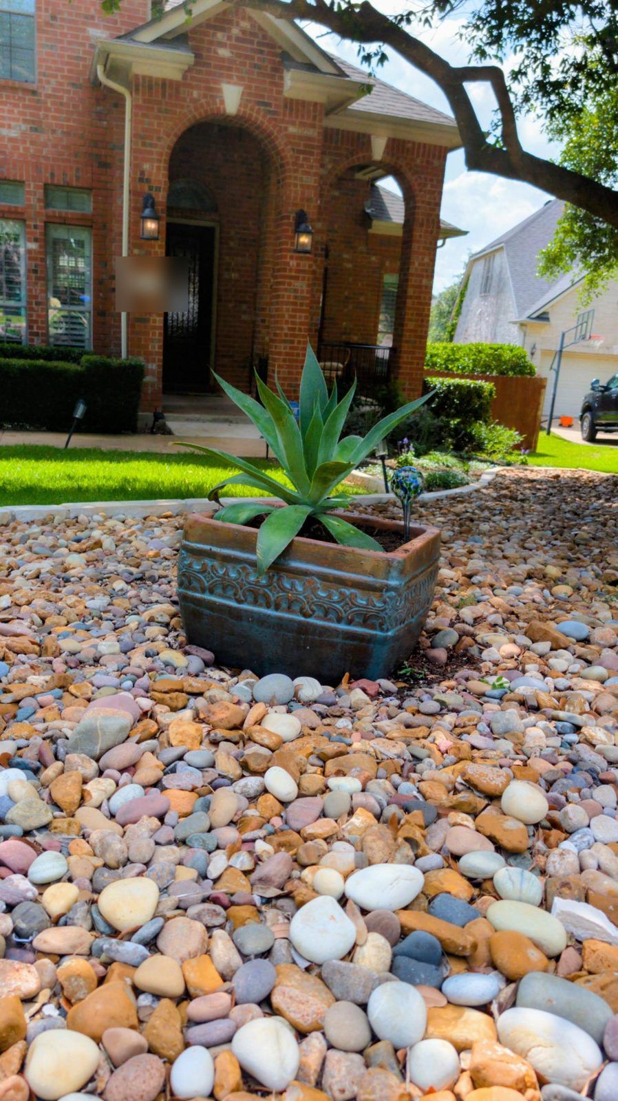 Agave in a glazed planter set in a bed of mixed river rock in a front yard