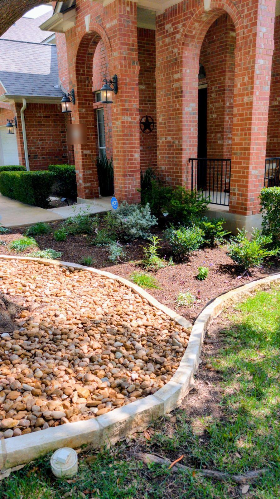 Front-yard bed of native shrubs and perennials in fresh mulch, edged with limestone and bordered by river rock